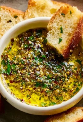 A bowl of garlic olive oil dip served with fresh bread and herbs.