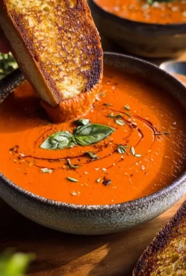 Bowl of creamy tomato soup garnished with fresh basil and drizzled with cream