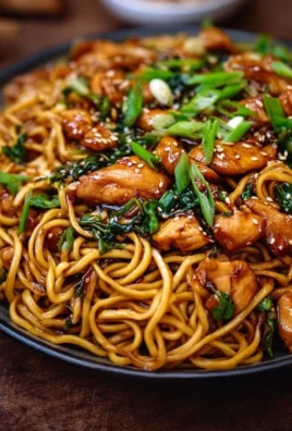 Plate of sticky garlic chicken noodles with fresh vegetables.