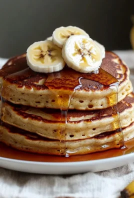 Fluffy banana pancakes stacked on a plate with syrup and fruits
