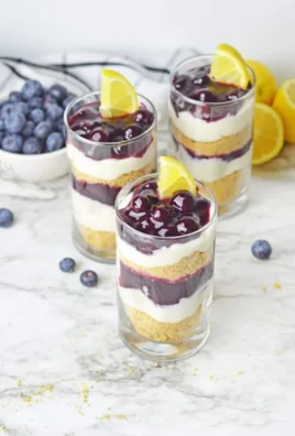 Lemon blueberry cheesecake parfait served in a glass with fresh blueberries and whipped cream.