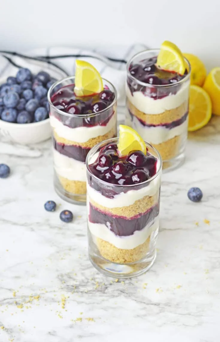 Lemon blueberry cheesecake parfait served in a glass with fresh blueberries and whipped cream.