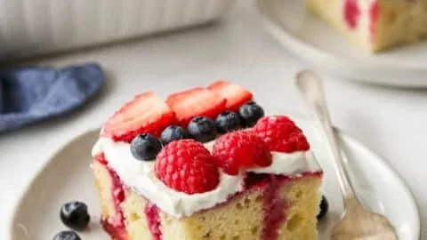 Delicious Berry Poke Cake topped with fresh berries and whipped cream