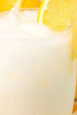 A glass of creamy lemonade topped with lemon slices and mint leaves.