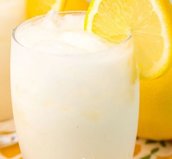 A glass of creamy lemonade topped with lemon slices and mint leaves.