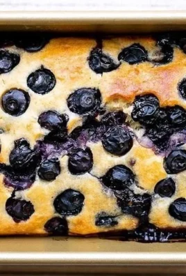 Slice of easy lemon blueberry bread with fresh blueberries on a wooden table