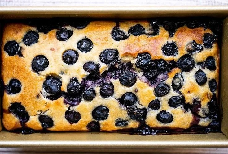 Slice of easy lemon blueberry bread with fresh blueberries on a wooden table