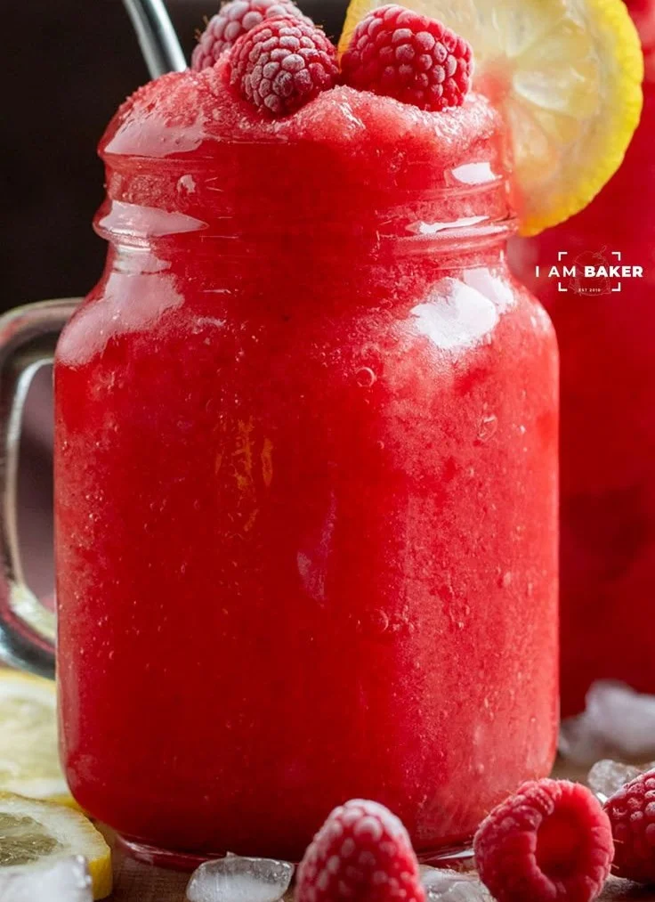 Delicious frozen raspberry lemonade in a glass, garnished with raspberries.