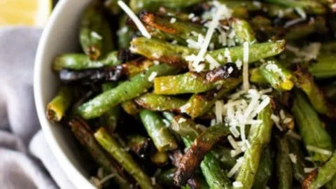 Plate of grilled garlic green beans on a rustic wooden table