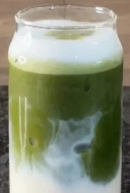 Iced Vanilla Matcha Latte served in a glass with a straw and matcha powder