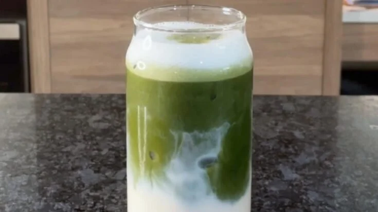 Iced Vanilla Matcha Latte served in a glass with a straw and matcha powder