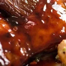 Delicious sticky grilled chicken garnished with herbs on a plate.